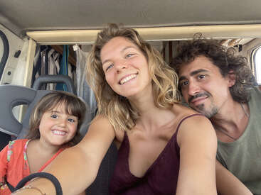 Une joyeuse famille de trois personnes, dont un enfant souriant, prend un selfie plein d'entrain à l'intérieur d'un camping-car, immortalisant ainsi un moment de joie et d'aventure.