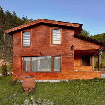 Une chalet en bois chaleureux, doté de grandes fenêtres, se dresse paisiblement au milieu d'une clairière. Entouré d'arbres et de collines, il dégage une atmosphère champêtre, à la fois sereine et rustique.