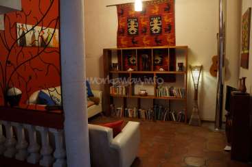 The image depicts a living room with a bookshelf, a white couch, and a red wall, featuring a unique blend of modern and traditional decor.
