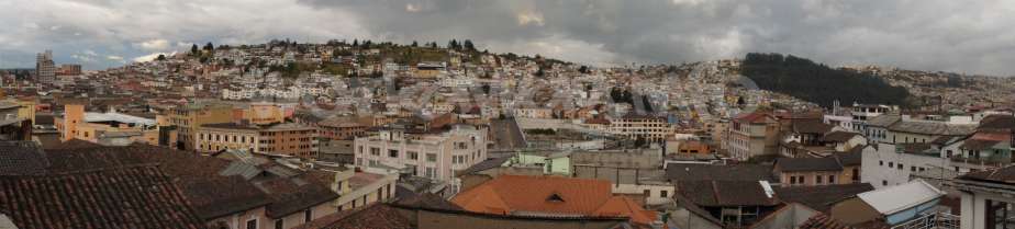 The image depicts a cityscape with a mix of buildings and rooftops, set against a cloudy sky. The cityscape is densely populated with a variety of structures.