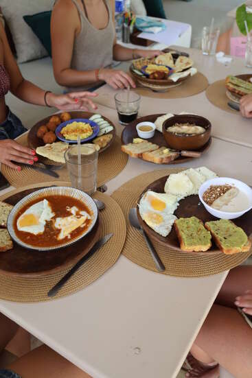 Four people are sitting around a table, enjoying a delicious brunch. The table is filled with eggs, avocado toast, bread, coffee, and assorted breakfast items.