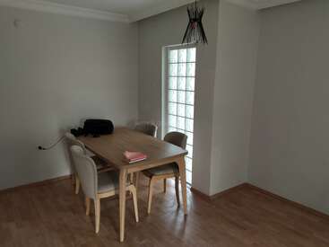 Uma sala de jantar minimalista com uma mesa de madeira, quatro cadeiras, um livro, uma bolsa, uma janela de bloco de vidro, piso de madeira e uma luminária preta moderna e exclusiva.