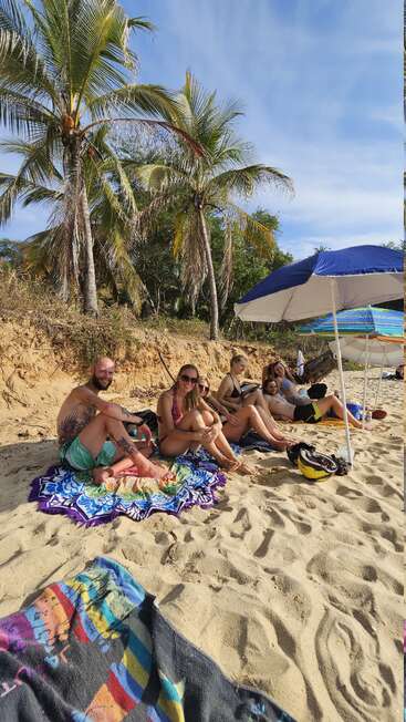 Eine Gruppe von Freunden entspannt sich an einem Sandstrand unter Palmen und Sonnenschirmen und genießt das sonnige Wetter und einen friedlichen, entspannten tropischen Nachmittag zusammen.