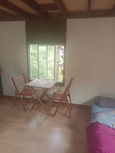 Ein gemütliches Zimmer mit Holzböden und -decken, einem kleinen Holztisch mit zwei Stühlen am Fenster und einem Bett mit buntem Bettzeug in der Nähe.