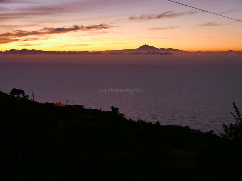 L'image représente un coucher de soleil serein sur une étendue d'eau, avec une chaîne de montagnes visible au loin, dans un ciel orange et jaune éclatant.