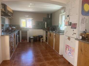 Il s'agit d'une cuisine confortable avec un sol carrelé brun, des armoires en bois, des comptoirs en granit, un dosseret vert, un grand réfrigérateur, un évier, une cuisinière, des bacs et beaucoup de lumière naturelle.