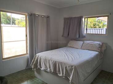 This is a simple, bright bedroom featuring a neatly made double bed with light bedding, two windows with curtains, and green-tiled floors. Minimalist and cozy.