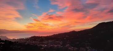 Un magnifique lever de soleil teinte le ciel de nuances roses, orangées et bleues. Des collines se découpant en silhouette et une ville paisible se nichent sous ce ciel nuageux aux couleurs époustouflantes.