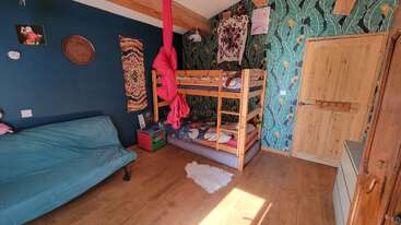 Cette chambre douillette comprend un lit superposé en bois, un papier peint vibrant, un futon bleu, des décorations colorées, un plancher en bois, un tapis moelleux et la lumière naturelle du soleil qui pénètre à l'intérieur.