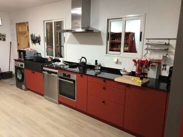 The image depicts a modern kitchen with red cabinets, black countertops, and stainless steel appliances, featuring a range hood, sink, and dishwasher.