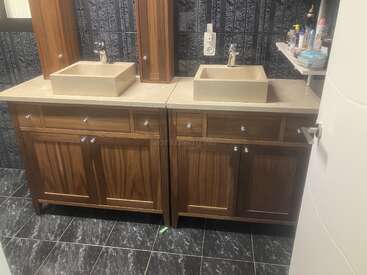 The image depicts a bathroom with two sinks and cabinets, featuring a white countertop, brown cabinets, and a black tiled floor, with a white door on the right side.