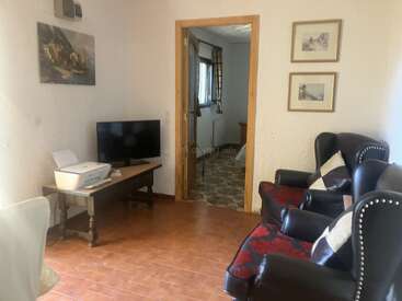 This cozy living room features two dark leather armchairs, a small TV on a wooden table, framed art, and a doorway leading to another room.