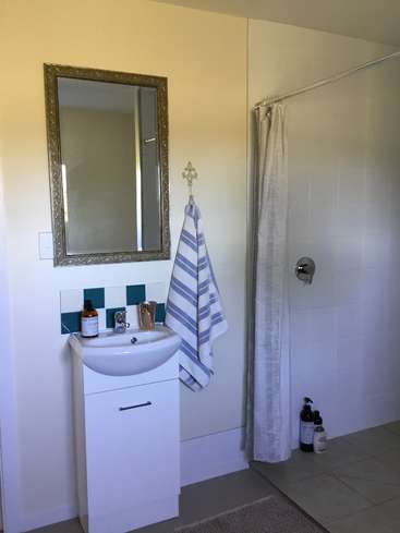 The image depicts a bathroom with a white sink, mirror, and shower, featuring a blue and white striped towel hanging from a hook on the wall.