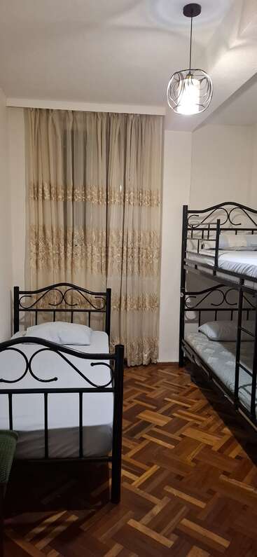 Dieses Zimmer hat ein Einzelbett und ein Etagenbett mit schwarzen Metallrahmen, Parkettboden, durchsichtige bestickte Vorhänge und eine moderne Deckenleuchte.