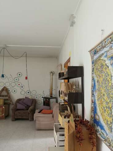 A imagem mostra uma sala aconchegante com paredes brancas, com um mapa, uma poltrona marrom, um sofá rosa e vários itens decorativos, criando uma atmosfera calorosa e convidativa.