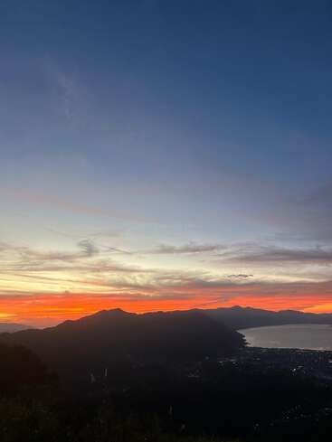 Um pôr do sol de tirar o fôlego pinta o céu com tons vibrantes de laranja e vermelho sobre montanhas em silhueta e um lago cintilante, criando uma cena de paisagem pacífica e serena.