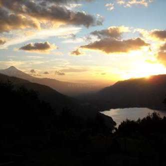 The image depicts a serene sunset over a lake, with mountains in the background and a cloudy sky, evoking a sense of peacefulness and tranquility.