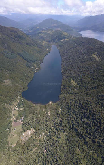 The image depicts a serene landscape featuring a large lake surrounded by lush green mountains and trees, with a small village nestled in the valley below.