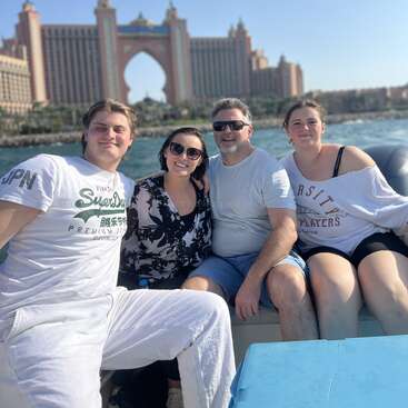 Quatre personnes, souriantes et détendues, sont assises ensemble sur un bateau, avec l'emblématique hôtel Atlantis, The Palm visible en arrière-plan sous le soleil, au bord de l'eau.