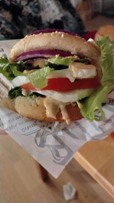 Gros plan sur un burger végétarien frais avec de la laitue, des tomates, des oignons, du fromage et de la sauce, tenu dans une main, enveloppé dans du papier journal. Appétissant et délicieux.