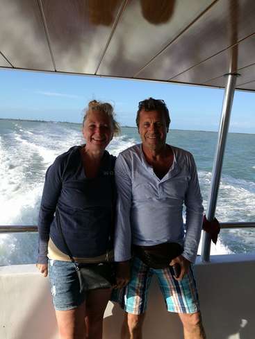Das Bild zeigt einen Mann und eine Frau, die auf einem Boot stehen, mit dem Meer und dem Himmel im Rücken. Sie tragen legere Kleidung und lächeln in die Kamera.