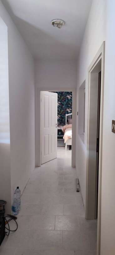 Das Bild zeigt einen Flur mit weißen Wänden und einer weißen Decke, mit einer Tür auf der linken Seite und einer Wand auf der rechten Seite, mit einer weißen Tür am Ende des Flurs.