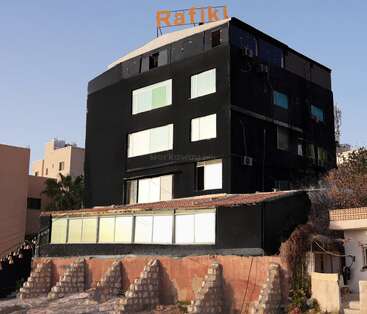 Ein schwarzes Gebäude mit großen Fenstern und einem orangefarbenen "Rafiki"-Schild auf dem Dach erhebt sich über ein niedrigeres Gebäude und Steinstufen.