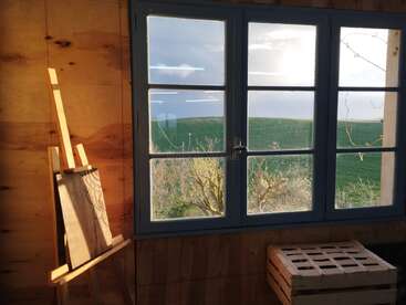 The image depicts a serene room with a large window overlooking a lush green field, featuring a wooden easel and crate, exuding a sense of calm and creativity.