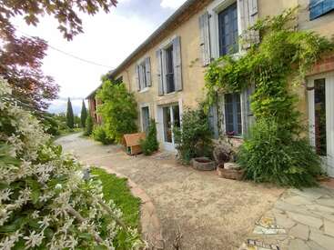 The image depicts a charming, two-story house with a warm, yellow exterior, adorned with lush greenery and a stone pathway leading to the entrance.