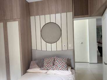 Une chambre confortable décorée avec des armoires en bois, un lit moelleux, des oreillers colorés et un mur circulaire unique. Une porte ouverte révèle un couloir lumineux.
