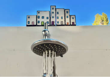 A showerhead releases water streams below a playful drawing of buildings, creating the illusion that water is flowing from the illustrated windows onto the viewer.