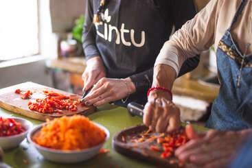Duas pessoas estão cortando pimentões vermelhos em tábuas de madeira em uma cozinha aconchegante. Você pode ver tigelas com cenouras raladas e ingredientes sobre a mesa.