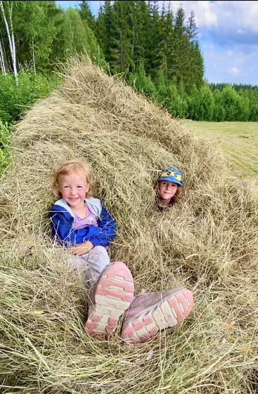 Par une journée ensoleillée, deux enfants s'amusent à s'asseoir et à se cacher dans un tas de foin, entourés d'arbres verdoyants et d'un magnifique paysage champêtre.