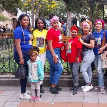 A group of women and a young girl pose together outdoors in a park, wearing colorful t-shirts with printed images, smiling and enjoying a casual gathering.