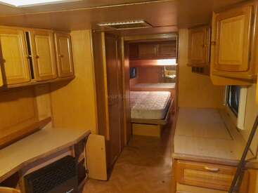 Esta imagen muestra el interior de una caravana. Cuenta con armarios con paneles de madera, una zona de trabajo y una cama en la parte trasera con compartimentos superiores.