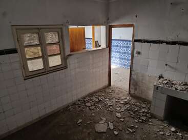 The image shows an abandoned room with broken tiles and debris on the floor. The walls are partially tiled, and there's a door leading to a blue-tiled room.