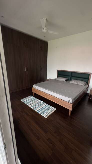 This bedroom features a large bed with two pillows, a striped rug, dark wooden floors, a ceiling fan, and a wall of built-in wardrobes.