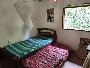 Cette chambre confortable dispose de deux lits, d'une literie aux couleurs vives, d'une moustiquaire et d'une fenêtre ouverte donnant sur un jardin luxuriant, ainsi que de décorations murales aux couleurs éclatantes.