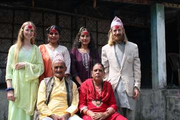 A family group, dressed in traditional Nepali attire, pose for a photo. They have tika on their foreheads, suggesting a celebration or festival occasion.