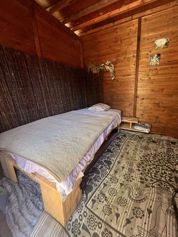 Este aconchegante quarto de madeira tem uma cama de solteiro com roupa de cama simples, um tapete estampado, decoração rústica e uma suave iluminação natural, criando um ambiente acolhedor, minimalista e tranquilo.