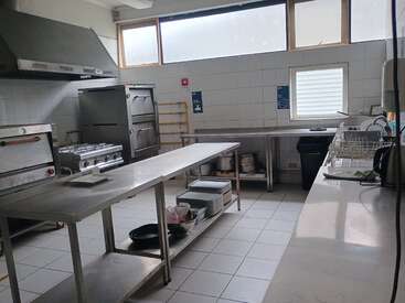 This image shows a clean, industrial kitchen with stainless steel counters, ovens, stove, dish rack, tiled walls and floor, and utensils neatly arranged on shelves.