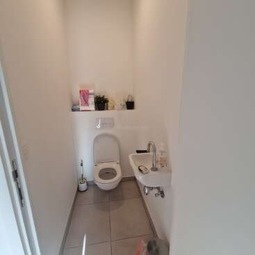 Les toilettes, petites et propres, aux murs blancs, sont équipées d'une cuvette murale, d'un minuscule lavabo avec du savon, d'une brosse de toilette et de produits d'hygiène posés sur une étagère.