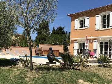 The image depicts a serene backyard scene featuring a pool, a house, and a statue of a person, set against a clear blue sky.