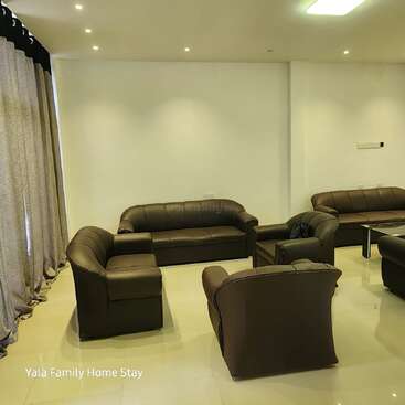 A modern living room with brown leather sofas arranged around a glass coffee table, cream-colored walls, large curtains, recessed lighting, and clean, shiny tile flooring.