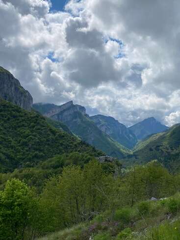 Majestuosas montañas verdes se elevan bajo un cielo espectacular lleno de densas y esponjosas nubes. El exuberante paisaje se extiende hasta perderse en la distancia, mostrando una belleza natural vibrante e intacta.