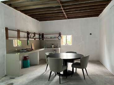 Cette photo montre une cuisine et un coin repas au style minimaliste, avec des poutres apparentes au plafond, une table ronde entourée de quatre chaises, des murs blancs, des étagères ouvertes et une petite fenêtre.