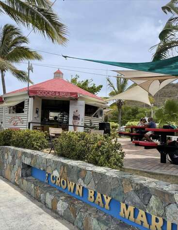 En el puerto deportivo de Crown Bay se encuentra una pintoresca cafetería llamada Scoops & Brew con techo rojo. Palmeras, bancos de picnic a la sombra y visitantes relajados crean un ambiente tropical.