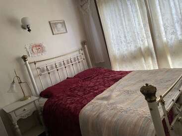 A cozy bedroom with a white vintage metal bed, red bedding, soft quilt, floral patterned curtains, ornate nightstand, wall décor, and a soft, warm ambiance.