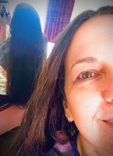 A woman takes a creative selfie, showing half her smiling face in the foreground, and her long hair from the back reflected in a mirror.