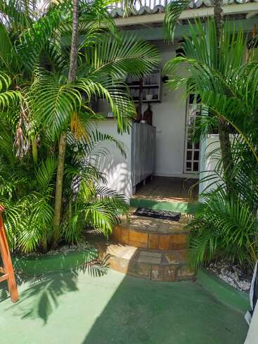 A small porch with tiled steps leads to a cozy white house entrance, surrounded by lush green palm plants, creating a tropical and inviting atmosphere.